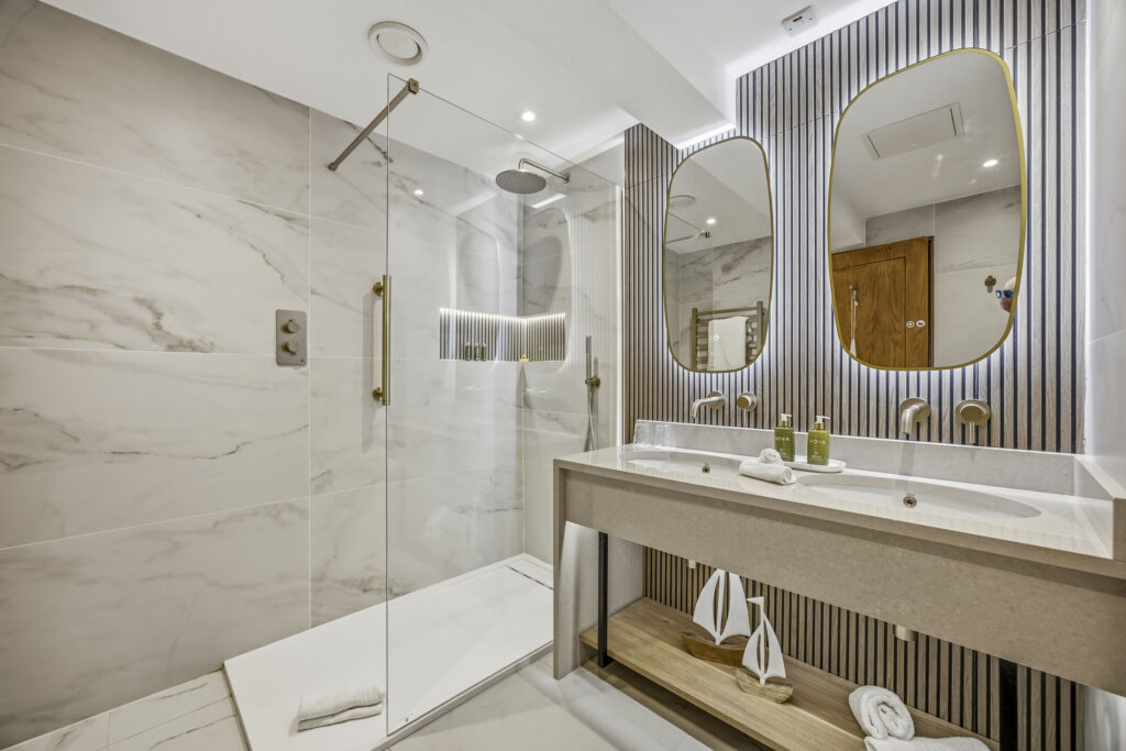 Elegant hotel bathroom with marble shower, twin sinks, and ambient lighting. Luxurious toiletries enhance your stay.