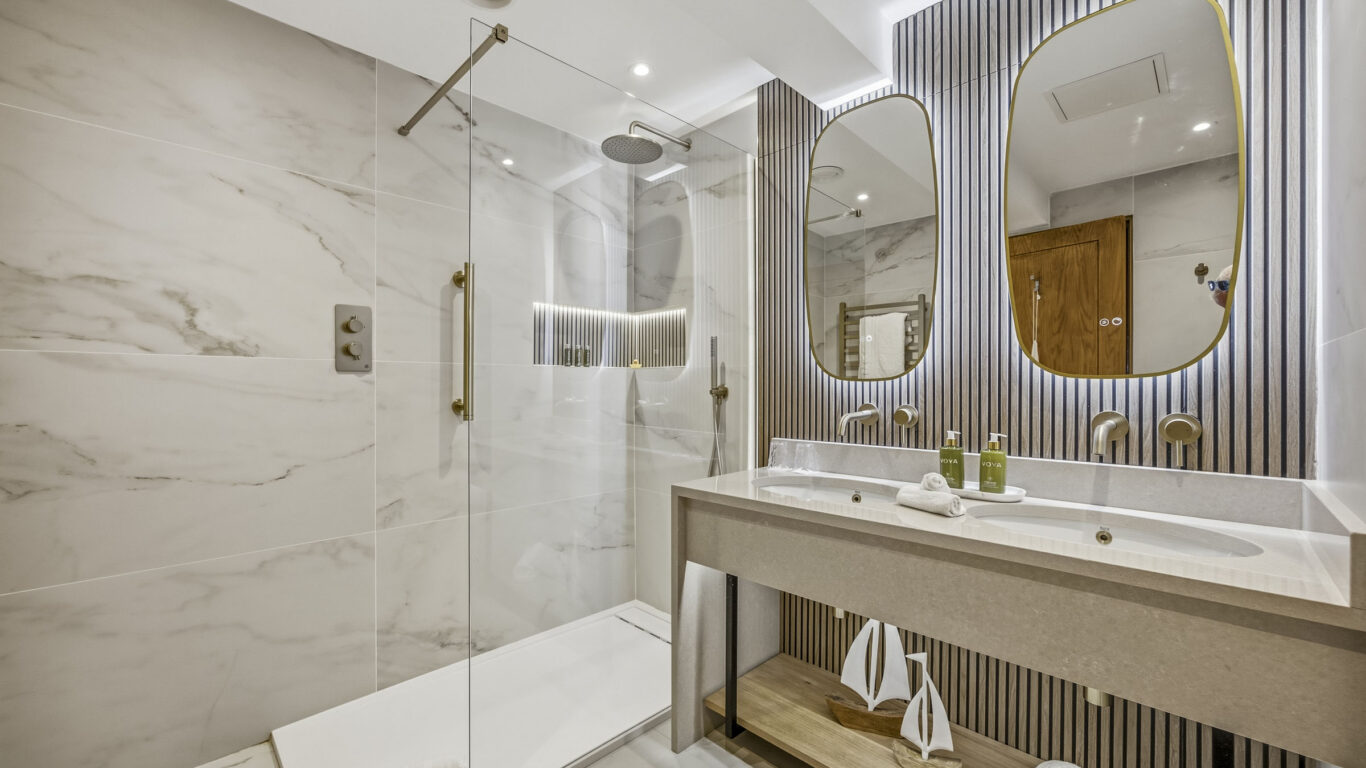 Elegant hotel bathroom with marble shower, twin sinks, and ambient lighting. Luxurious toiletries enhance your stay.