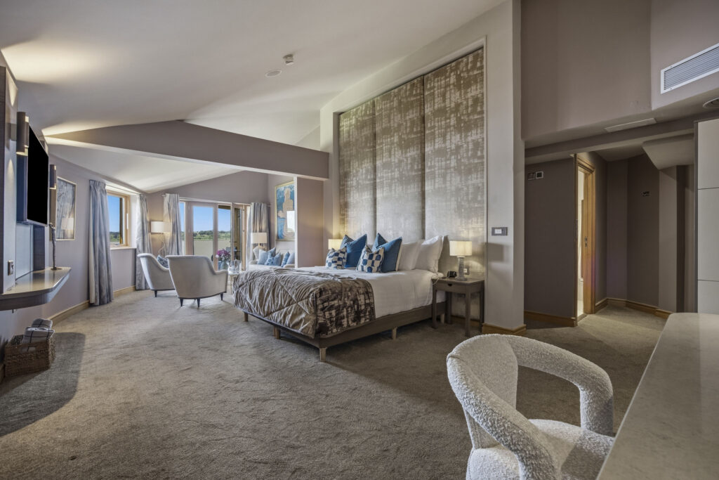 Spacious deluxe hotel room with king bed, modern decor, seating area, scenic views through large windows.