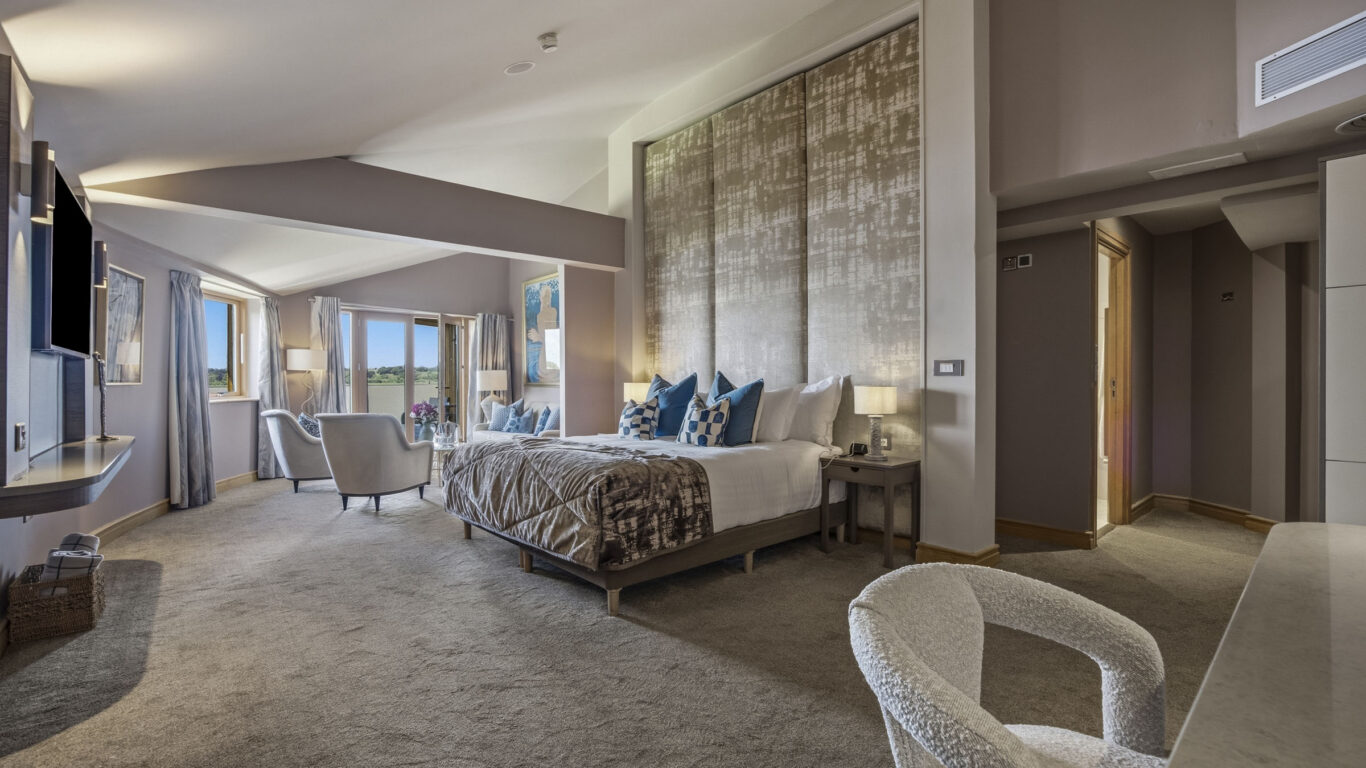 Spacious deluxe hotel room with king bed, modern decor, seating area, scenic views through large windows.