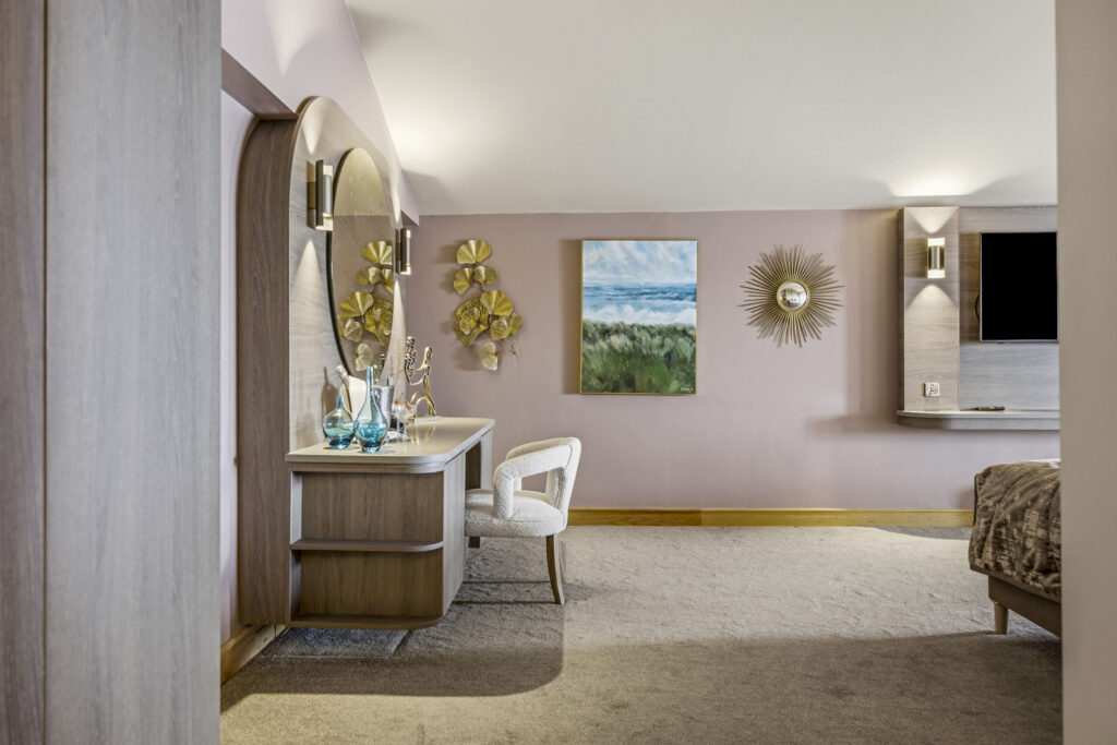 Elegant hotel room with soft pink walls, stylish decor, a plush chair, and wall art. Perfect for a relaxing stay.