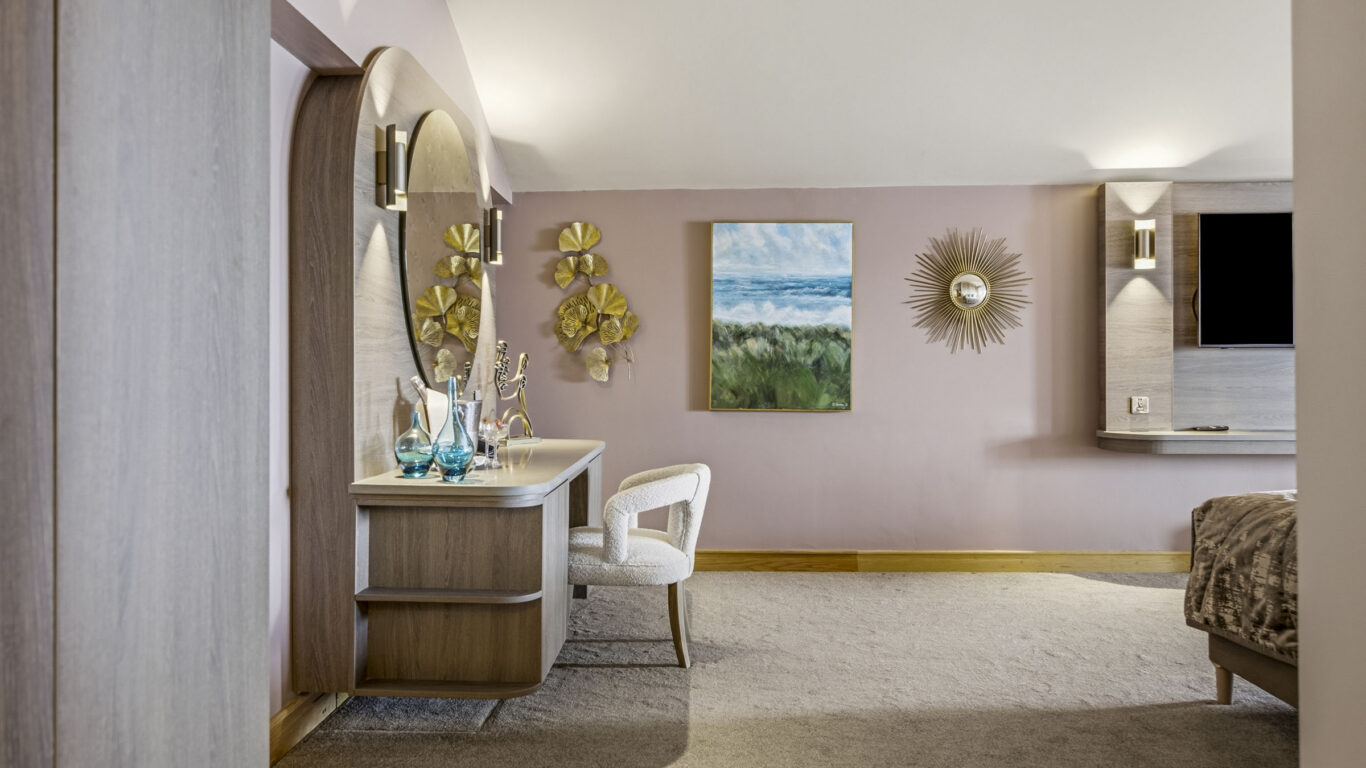 Elegant hotel room with soft pink walls, stylish decor, a plush chair, and wall art. Perfect for a relaxing stay.