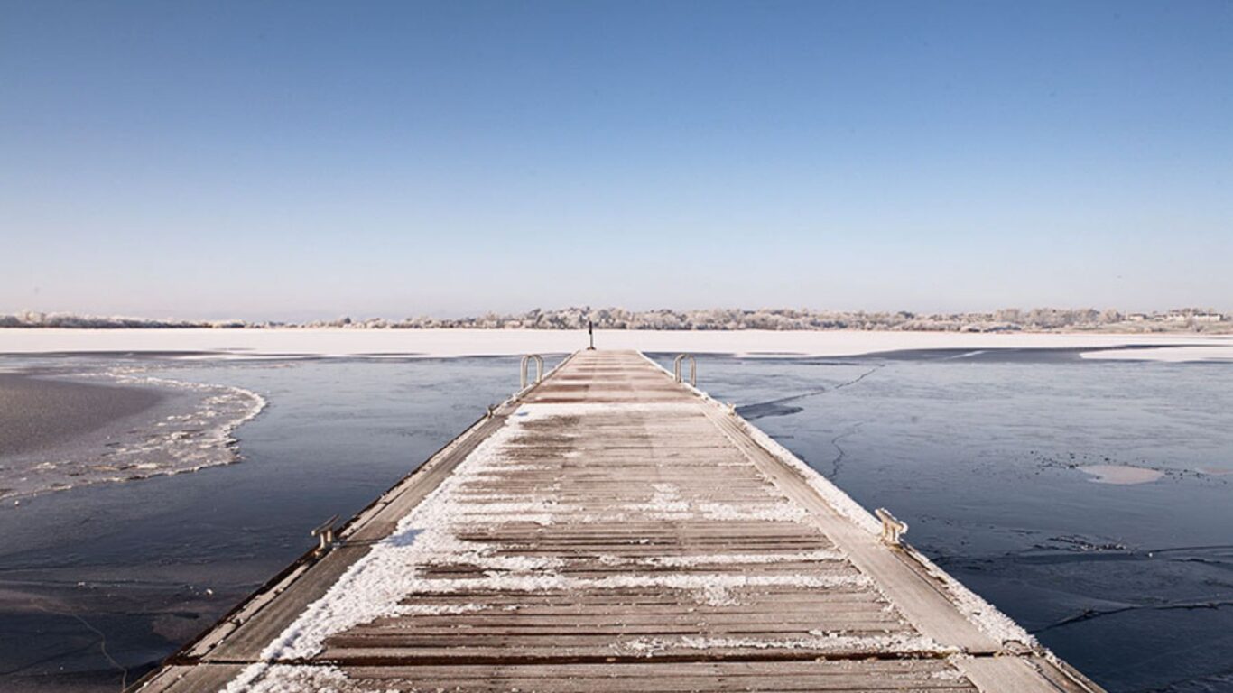 Serene snowy pier extending over a frozen lake under clear skies, inviting in winter's tranquillity.