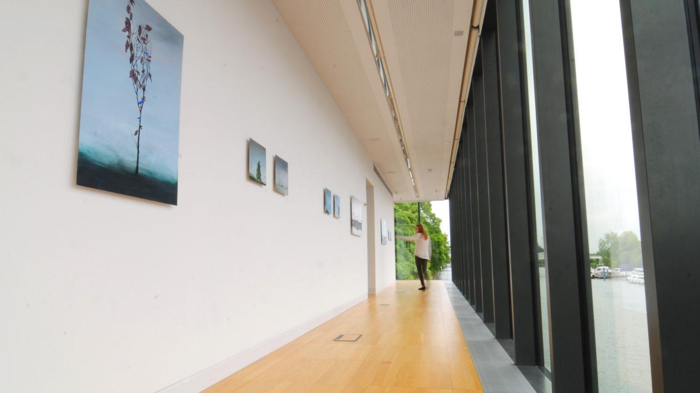 Elegant hotel corridor with art gallery, floor-to-ceiling windows, scenic river view, and a serene, inviting atmosphere.