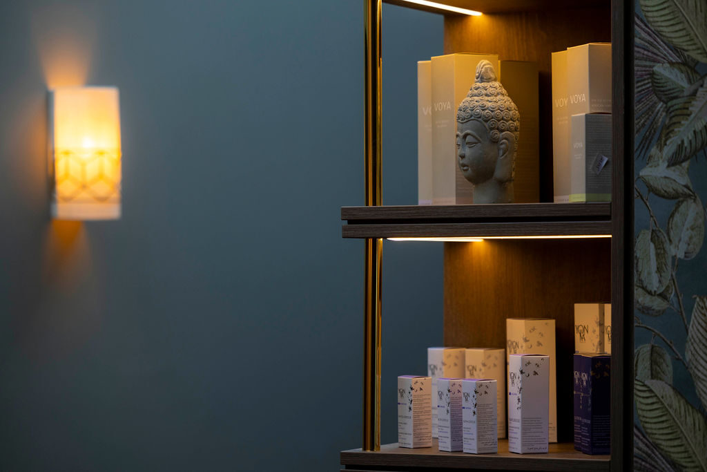 Soft-lit wellness display with Buddha statue and luxury skincare, inviting relaxation and tranquillity in serene spa setting.