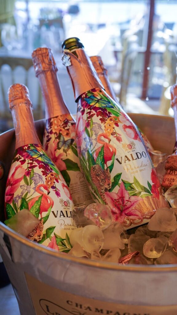 Vibrant bottles of Valdo Prosecco on ice, with floral design, set against elegant dining setting, promising a luxurious stay.