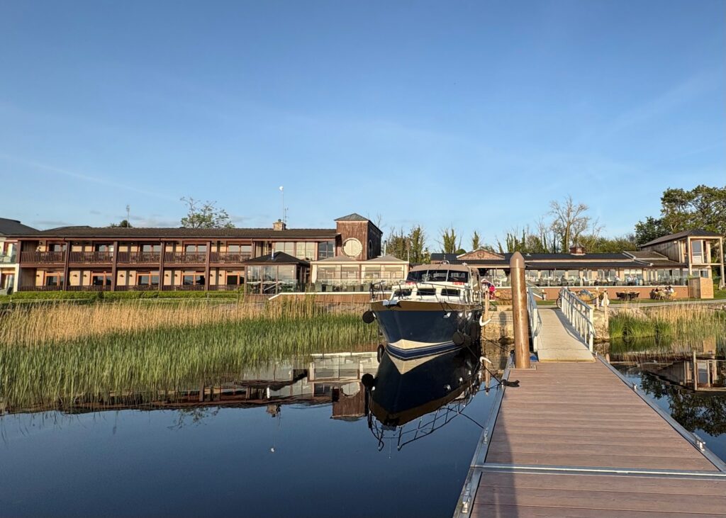 Scenic hotel by the lake with boat dock, modern glass dining area, lush greenery, offering serene waterfront views.