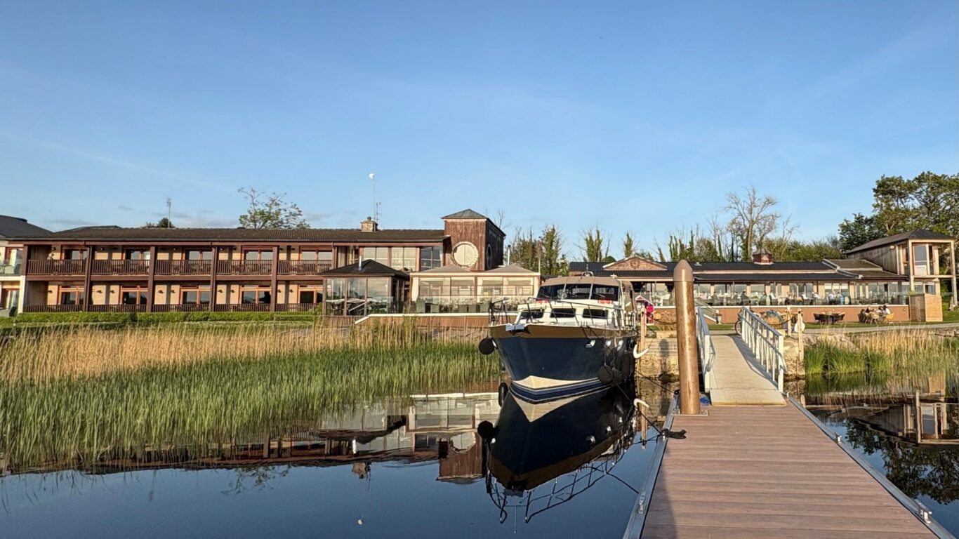 Scenic hotel by the lake with boat dock, modern glass dining area, lush greenery, offering serene waterfront views.