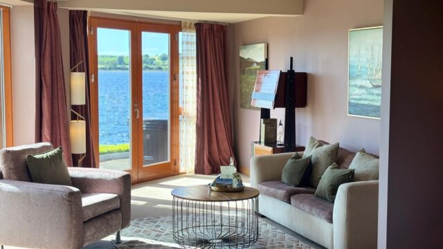 Cosy hotel suite with plush seating, lake view through large windows, elegant decor, inviting relaxation.