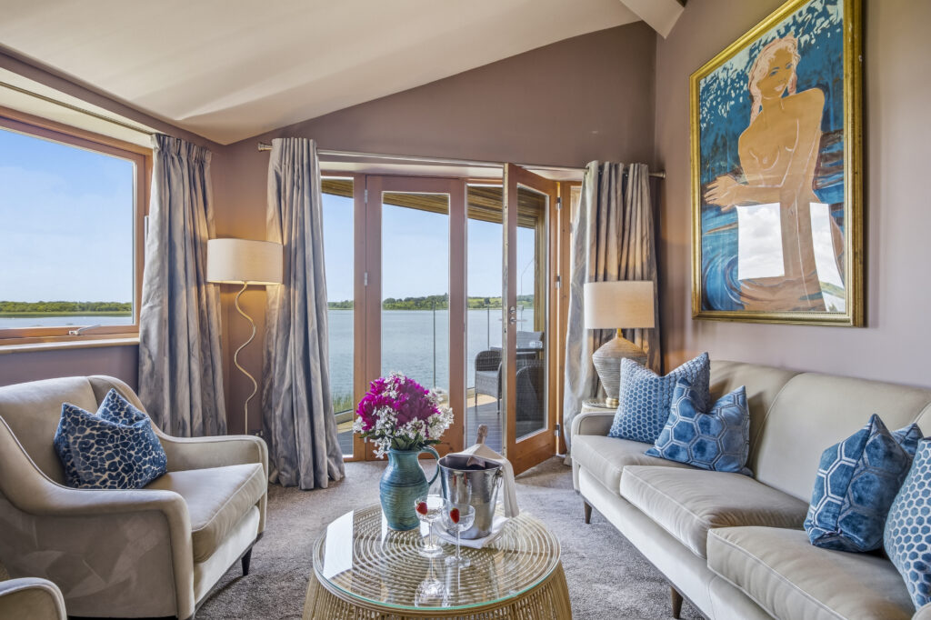 Spacious hotel suite with lake view, elegant decor, plush seating, modern art, and fresh flowers.