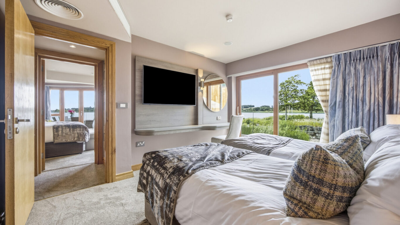 Spacious hotel room with lake view, twin beds, modern d&eacute;cor, and a flat-screen TV, offering a serene and cosy stay.