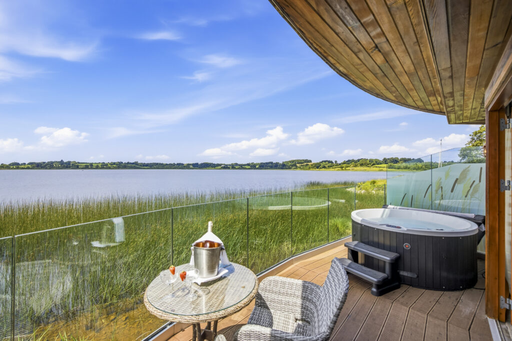 Luxurious lake view balcony with private hot tub and seating, perfect for relaxation and scenic nature enjoyment.