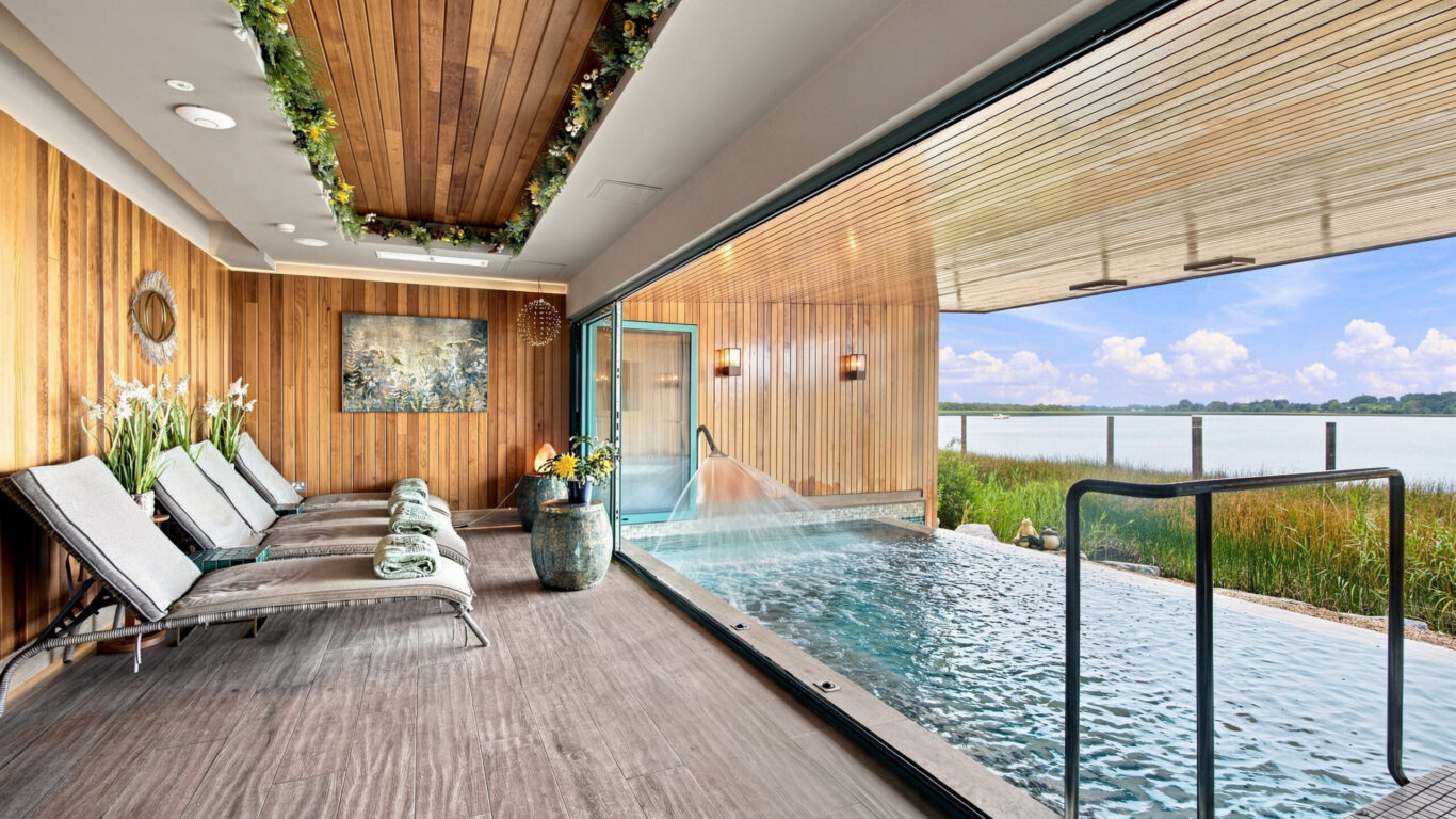 Luxurious spa room with wooden loungers, greenery, indoor pool, and lake view, offering relaxation and tranquility.